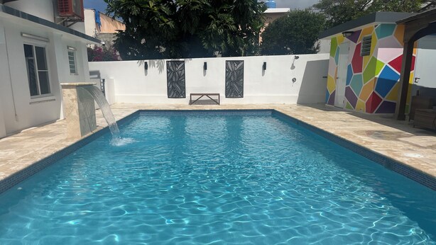 A rectangular swimming pool with clear blue water, surrounded by a white wall with decorative panels and a colorful wall to the right. - Sea Breeze Tunnel Hideaway 6 (Terranova)