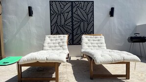 Two white cushioned lounge chairs with wooden frames, positioned in front of a wall with a black and white leaf pattern. - Sea Breeze Tunnel Hideaway 6 (Terranova)