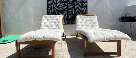 Two white cushioned lounge chairs with wooden frames, positioned in front of a wall with a black and white leaf pattern.