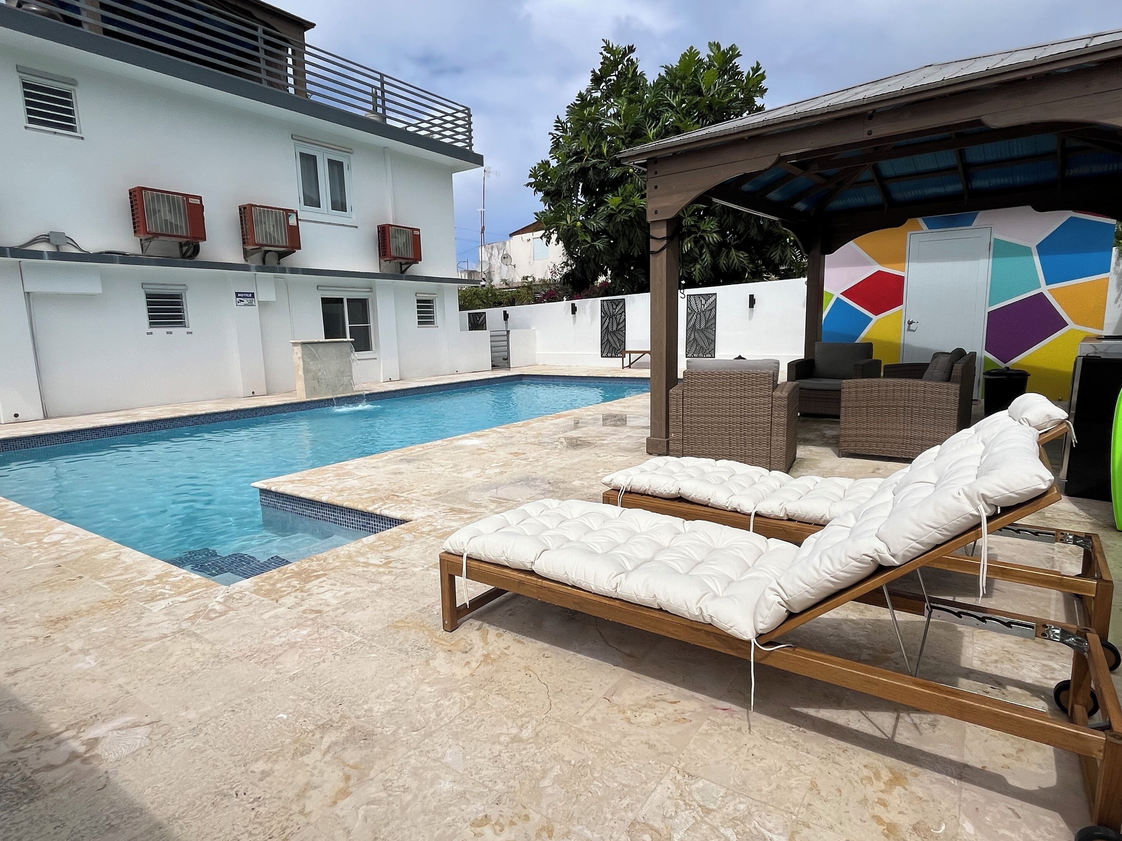 A swimming pool with lounge chairs, a covered seating area, and a colorful wall.