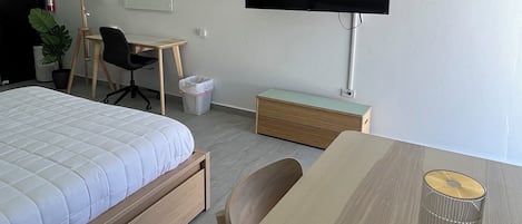 Una habitación de hotel moderna con cama, escritorio, silla, televisor y una mesita con un vaso y una botella.