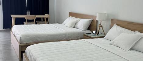Una habitación de hotel con dos camas, un escritorio, una silla, aire acondicionado y una lámpara.