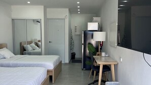 A modern hotel room with two beds, a desk, a chair, a trash bin, and a refrigerator. - Sea Breeze Tunnel Hideaway 6 (Terranova)