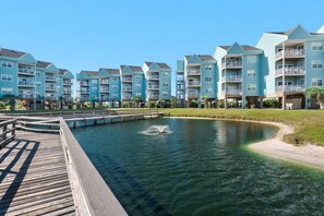 A waterfront residential building with multiple balconies, a wooden dock, and a small water feature.