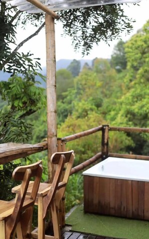 A wooden deck with a hot tub and chairs, surrounded by lush greenery and trees.