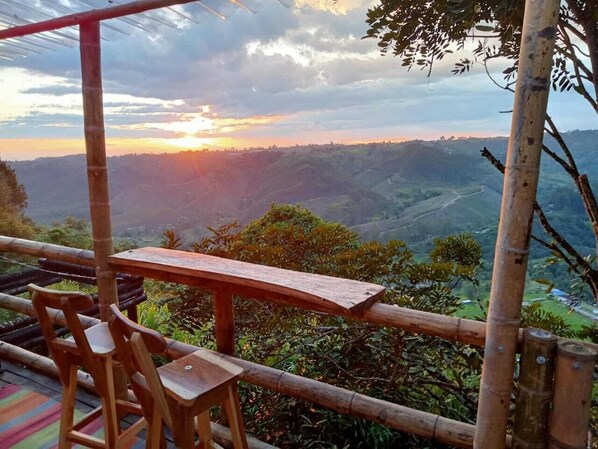 A wooden table and chairs set on a bamboo railing overlooking a valley.
