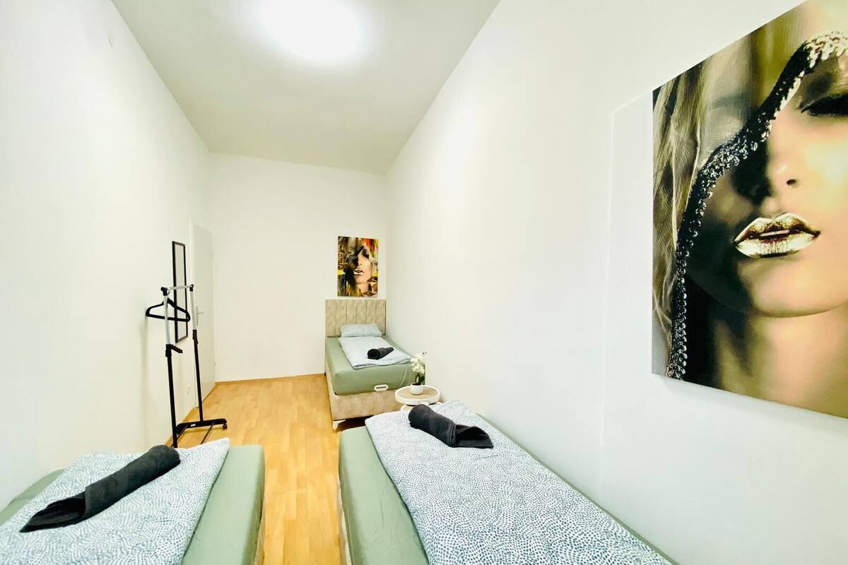 A room with two beds, a standing mirror, a painting, and a wooden floor.