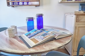 Ein runder Holztisch mit einer Zeitschrift, zwei blauen Glasflaschen und zwei weißen Tassen mit italienischen Motiven.