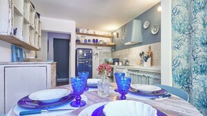 A dining area with a wooden table set for four, blue glassware, and a vase with red flowers. - La Medusa Blu (Albenga)