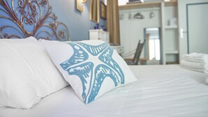 A neatly made bed with white and blue patterned pillows, a metal headboard, and a view of a bathroom with a mirror and towel rack. - La Medusa Blu (Albenga)