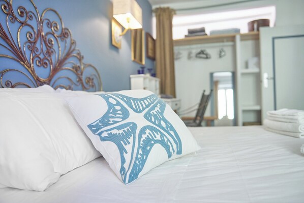 Un lit bien fait, avec une literie blanche et un oreiller bleu orné de motifs en forme d’étoiles, une tête de lit en métal et une vue sur une salle de bain avec un porte-serviettes.
