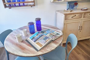 A round wooden table with two white mugs, two blue glass jars, and an open magazine with photos. - La Medusa Blu (Albenga)