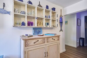 Una habitación con un armario de madera, una estantería con diversos objetos y una cesta de ropa.