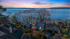 A residential area with houses near a large body of water, likely a lake or sea, during sunset. - Dash Point Retreat by the Beach with Amazing Water Views from Almost Every Room. (Tacoma)