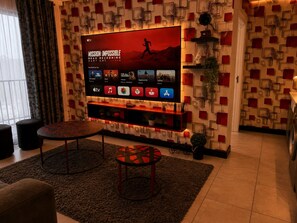 A living room with a large flat-screen TV mounted on a wall, a coffee table, a sofa, and a patterned wall design.