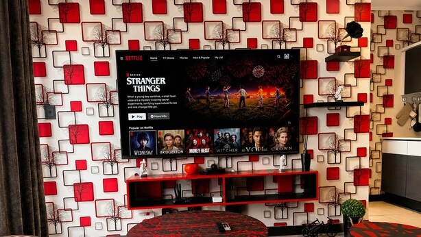 Ett modernt vardagsrum med en platt-TV som visar en serie från Netflix, en röd och svart mönstrad vägg och en minimalistisk möblering.