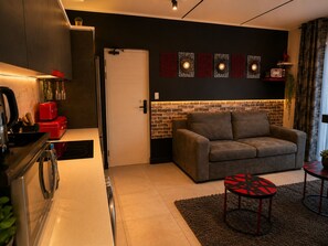 A modern living space with a kitchen, a sofa, and a small table. - Ruby Nest: Modern Smart Living (Midrand)