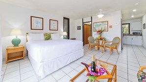 A hotel room with a large bed, a small dining table with chairs, a kitchenette, and a bathroom visible through an open door.