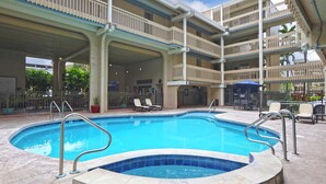 A swimming pool with a hot tub, surrounded by a covered patio with lounge chairs and a bar area.