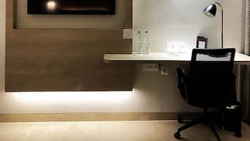 A modern office space with a mounted TV, a desk with a chair, a desk lamp, and two bottles of water.