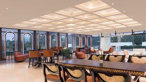 Un comedor amplio con una mesa larga y múltiples sillas, ventanas grandes con marcos decorativos y un diseño moderno de techo.