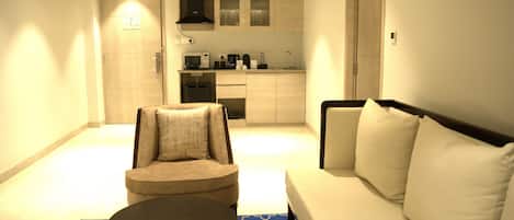 A compact living space with a sofa, a small armchair, a coffee table, and a kitchenette in the background.