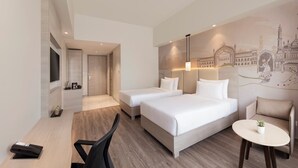Habitación de hotel con dos camas, un escritorio, una silla, una mesita, un televisor y un mural en la pared.