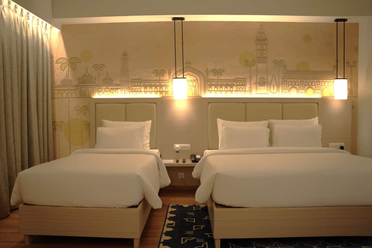 Habitación de hotel con dos camas, una mesita de noche y un mural en la pared.