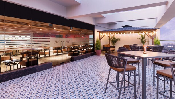 Un bar en la azotea con mesas al aire libre, suelo estampado y vistas de la ciudad.