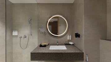 A modern bathroom with a granite countertop, a round mirror, a handheld showerhead, and a towel rack.