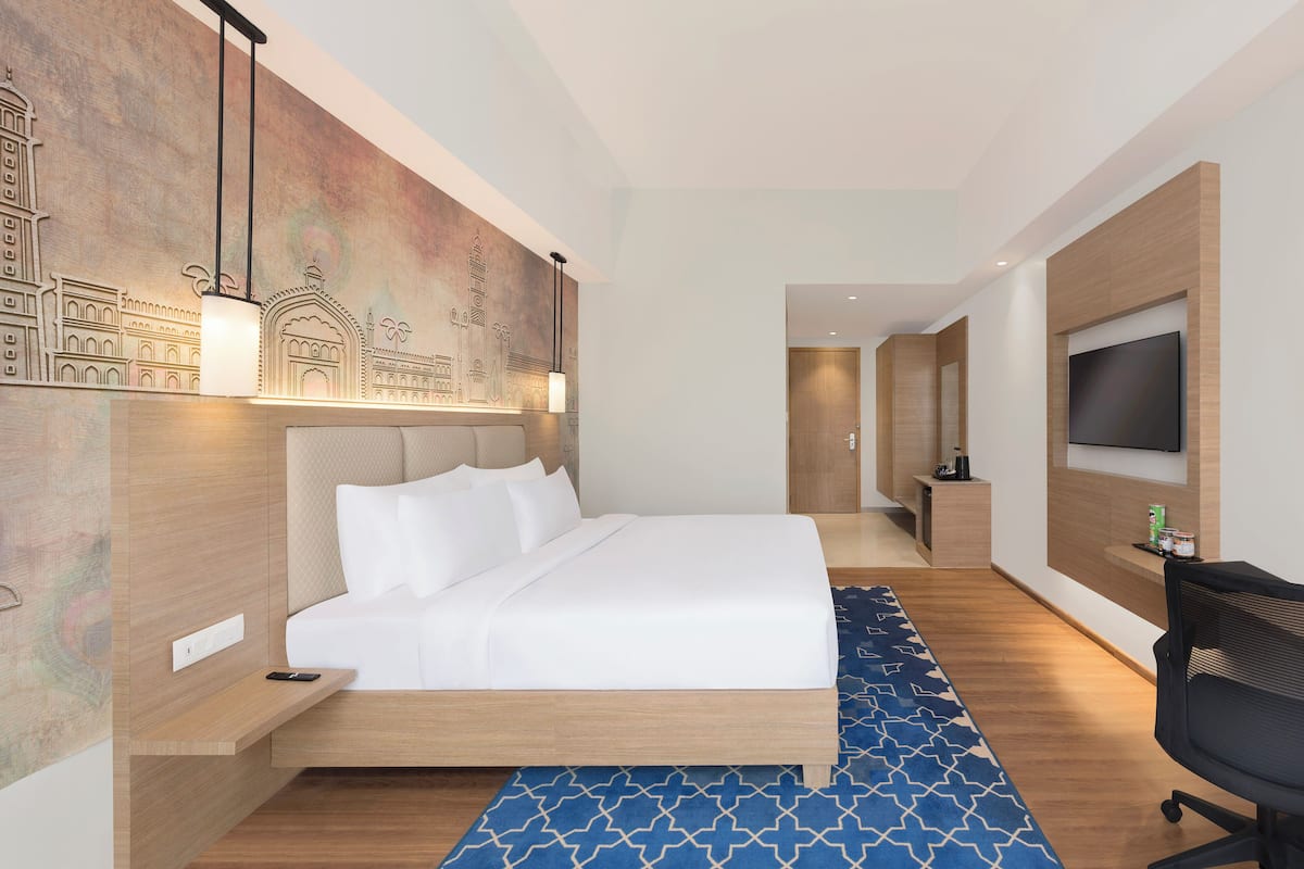 Una habitación de hotel moderna con una cama grande, un televisor de pantalla plana montado en la pared y un escritorio con una silla.