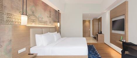A modern hotel room with a large bed, a flat-screen TV mounted on the wall, and a desk with a chair.
