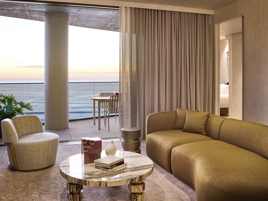 A modern living room with a sofa, armchair, and a coffee table. A balcony with a view of the sea is visible.