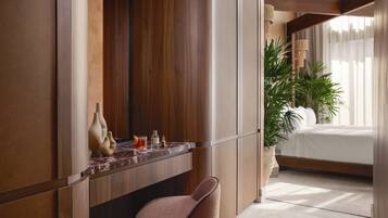 A modern hotel room with a wooden vanity, a marble countertop, a plush chair, a large potted plant, and a neatly made bed.