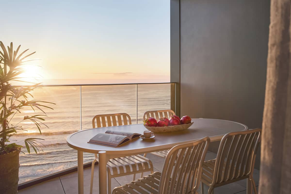 A balcony with a table, chairs, a bowl of fruit, and a plant.