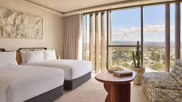 A hotel room with two beds, a sofa, a round wooden table, and a large window with a city view.