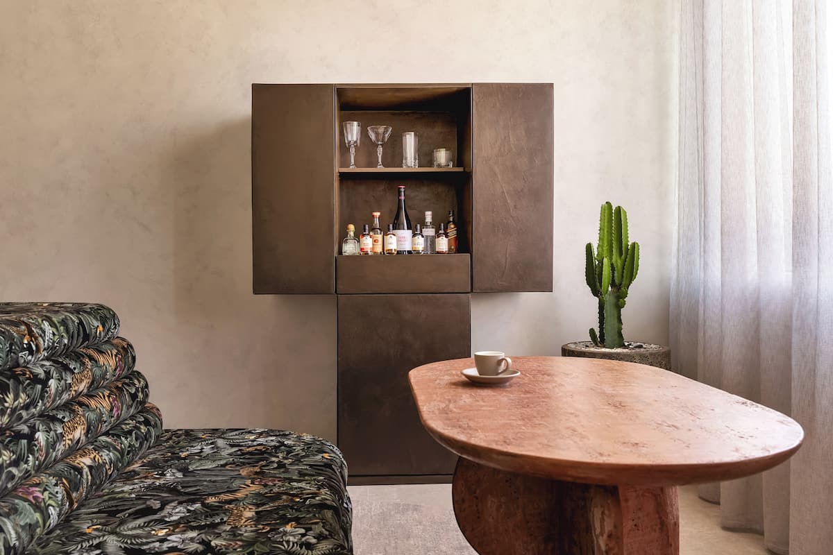 A modern living room with a patterned sofa, a wooden coffee table, a cabinet with liquor bottles, and a cactus plant.