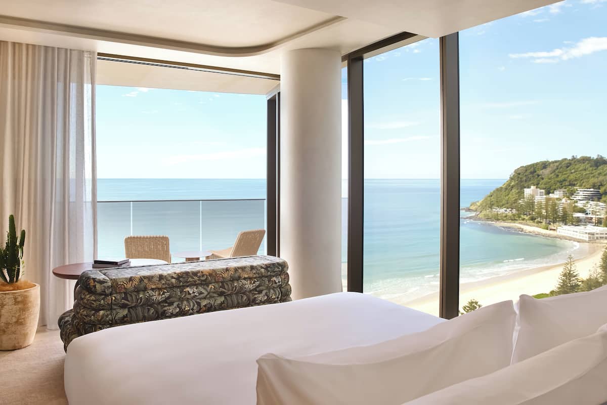 A hotel room with a large window offering a view of the beach and ocean.
