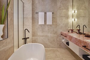 A modern bathroom with a freestanding bathtub, a large mirror, and a marble countertop with two sinks.