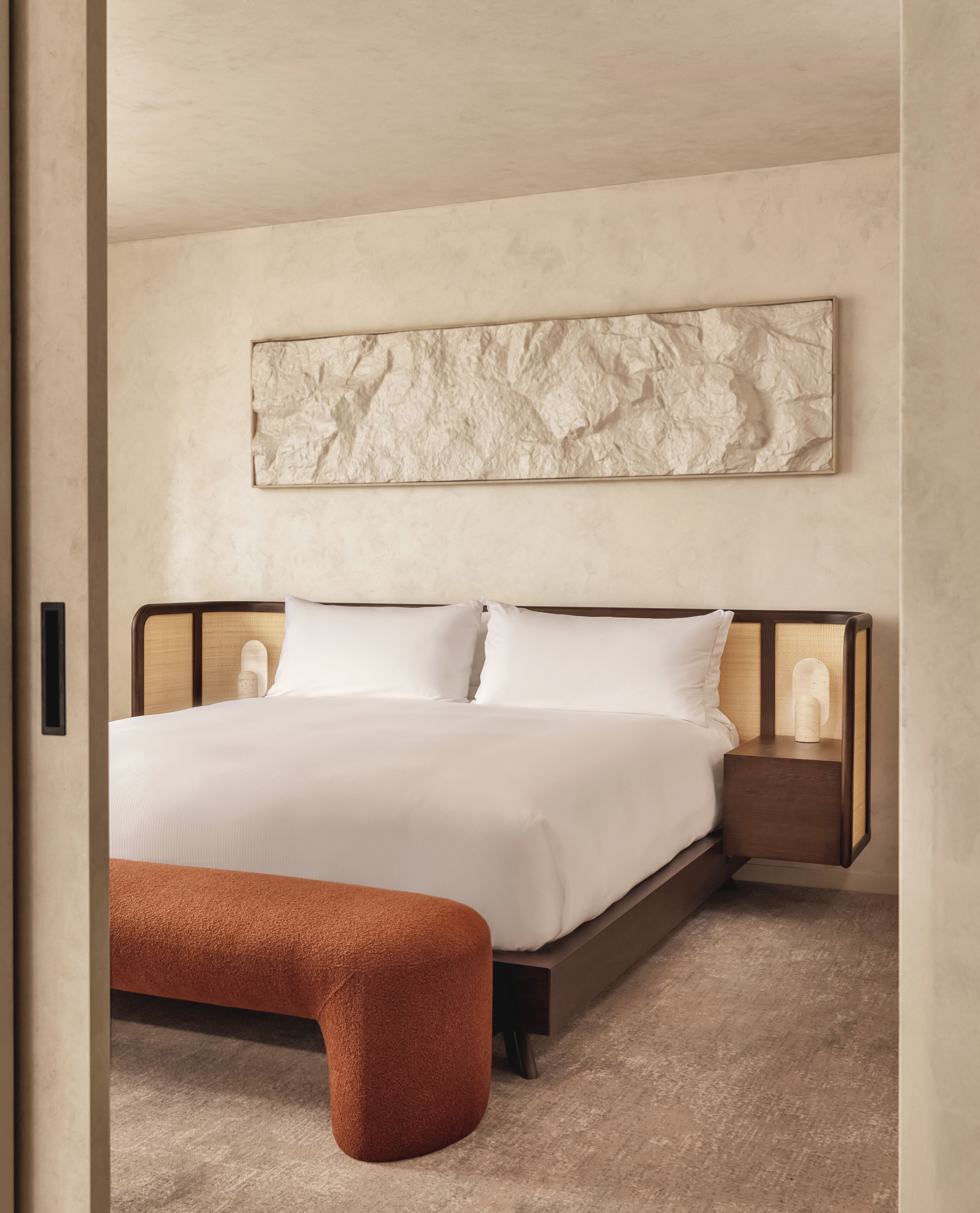 A modern bedroom with a large bed, a nightstand, and a bench.