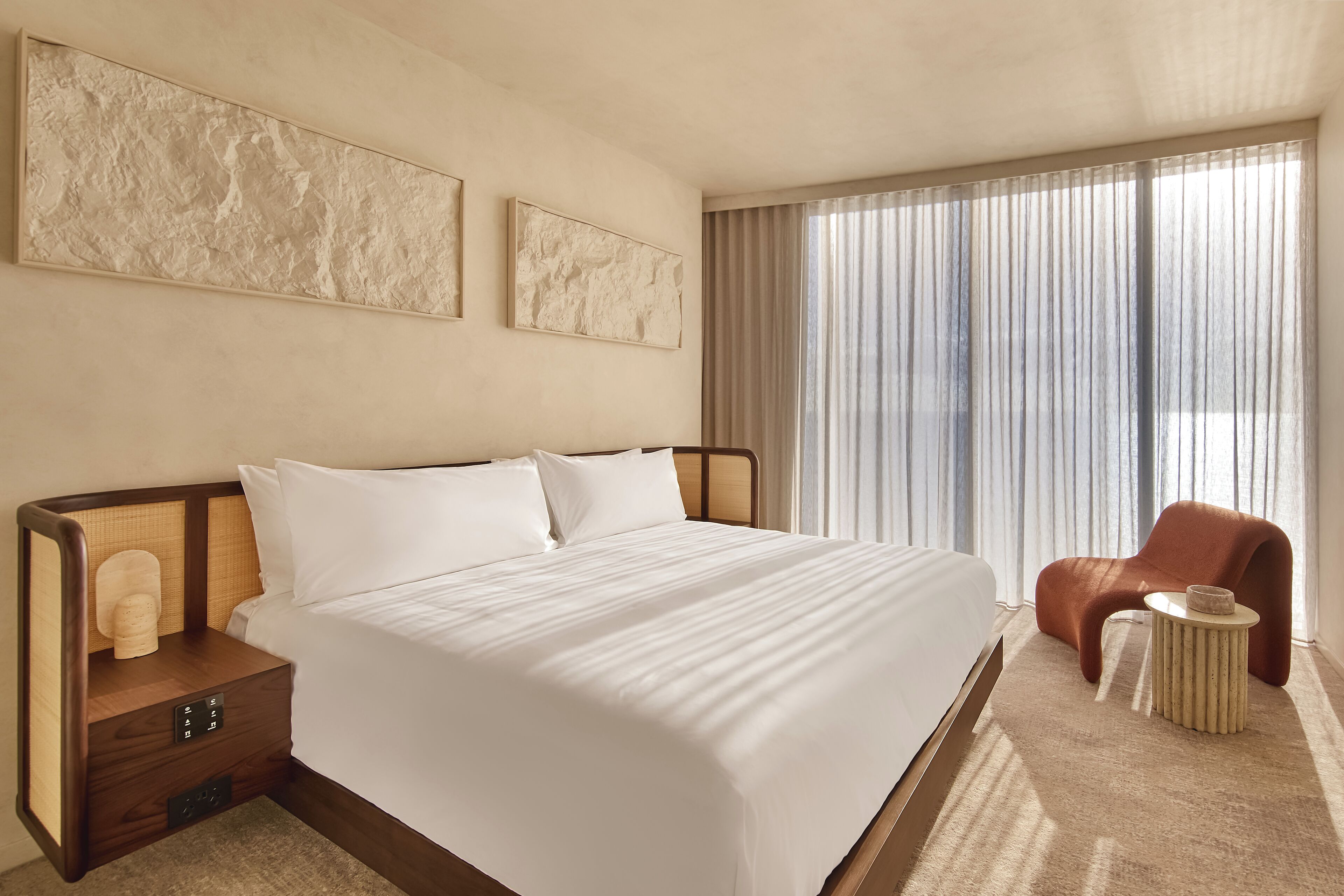 A hotel room with a large bed, a nightstand with a lamp, a chair, and a window with curtains.
