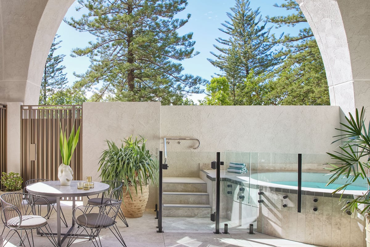 A patio area with a round table, chairs, a hot tub, and a staircase leading to an upper level.