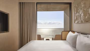 A hotel room with a bed, a view of the sea, and a large window with curtains.