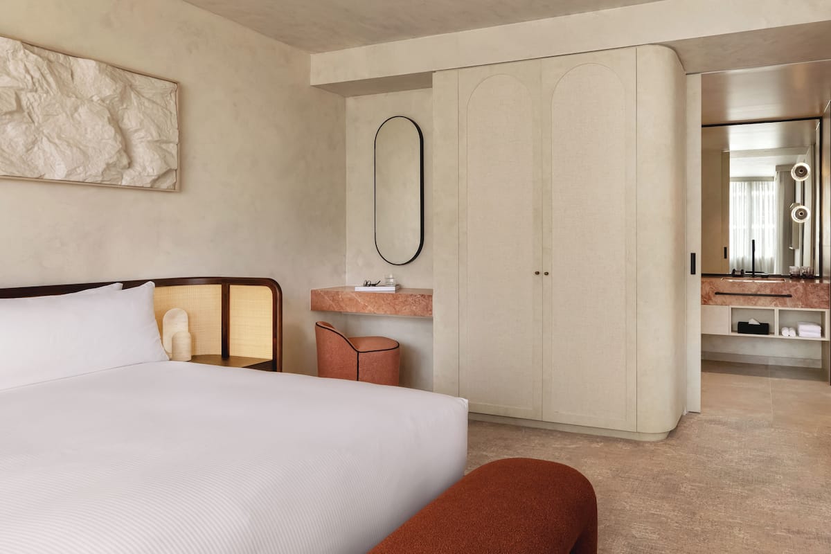 A modern hotel room with a large bed, a vanity with a mirror, and a wardrobe.