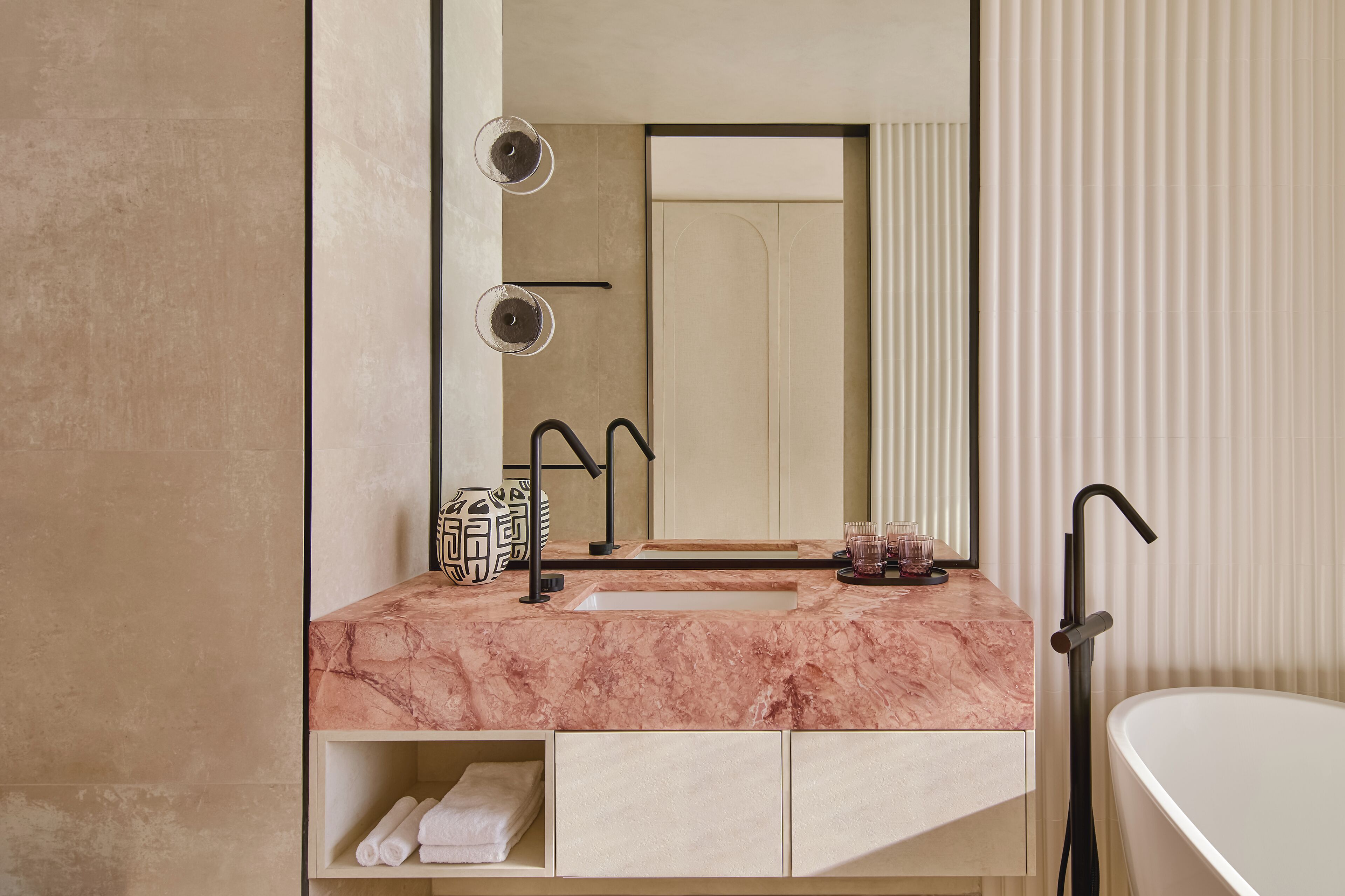 Un baño moderno con lavamanos de mármol, un espejo grande, un perchero para toallas y una bañera.