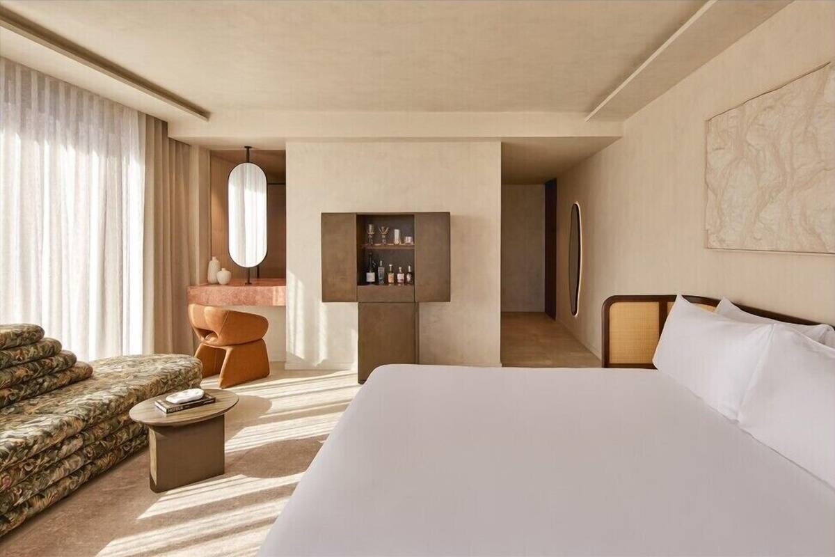 A modern hotel room with a large bed, a sofa, a small round table, a vanity with a mirror, and a cabinet with toiletries.