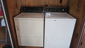 A laundry room with two stacked washers and dryers, wooden walls, and a broom leaning against the wall. - Charming 3-bedroom, 2 bath-room house with WiFi and AC in Lewes. (Lewes)