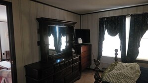 A room with a large wooden dresser, a television on top, a mirror, and a bed with a green blanket. - Charming 3-bedroom, 2 bath-room house with WiFi and AC in Lewes. (Lewes)