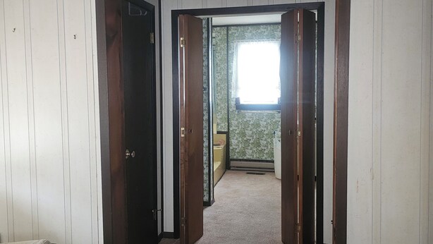 A room with a bed, a wooden door, and a hallway leading to another room with a window. - Charming 3-bedroom, 2 bath-room house with WiFi and AC in Lewes. (Lewes)