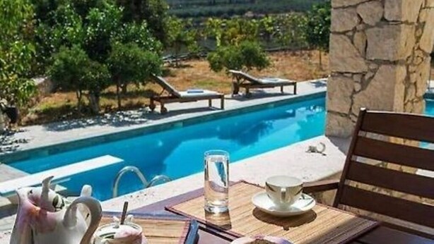 A poolside table with a teapot, cups, and a glass of water, overlooking a pool and lush greenery. - Panorama Luxury Villa in Sitia, Crete (Sitia)